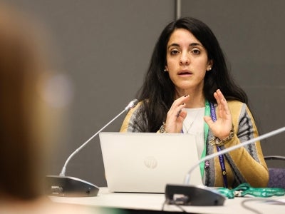 Woman gesturing in front of laptop on a panel